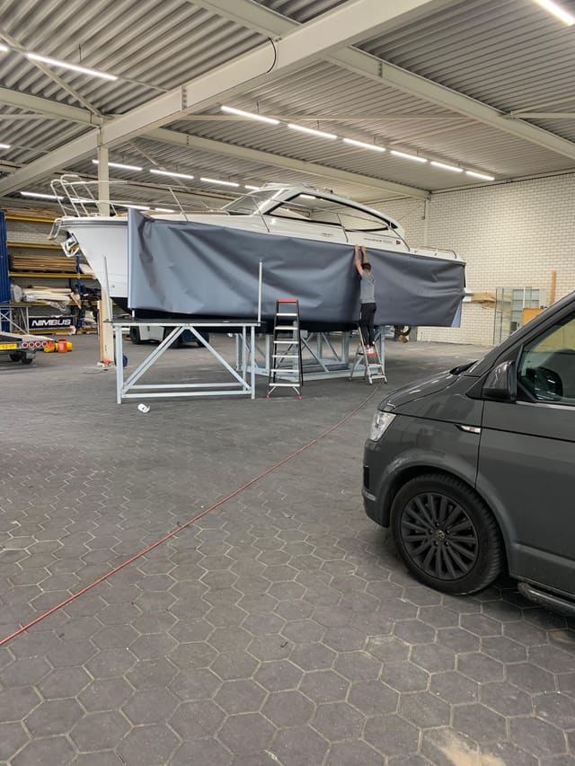 Een motorboot wordt in de loods in donkergrijze folie gezet