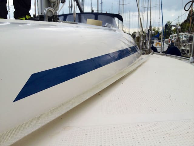 Donkerblauwe sierstreep langs de kajuitopbouw van een witte zeilboot, gezien vanaf het dek