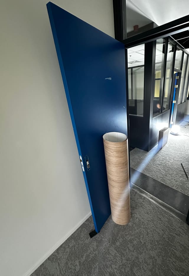 Donkerblauwe deur vóór het wrappen, met een rol houtlookfolie ertegen