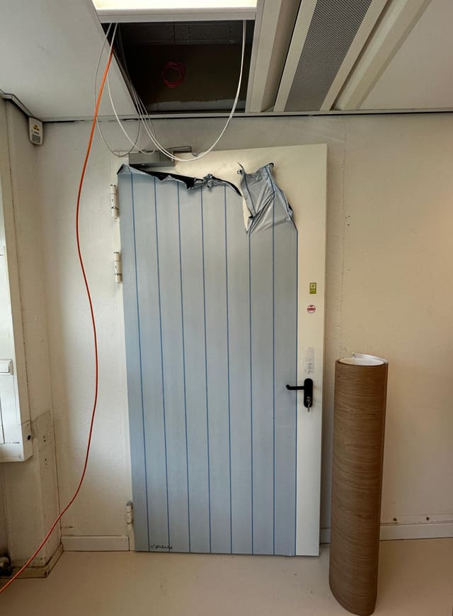 Lichtblauwe deur vóór het wrappen, met de oude laag half los en een rol houtlookfolie ernaast