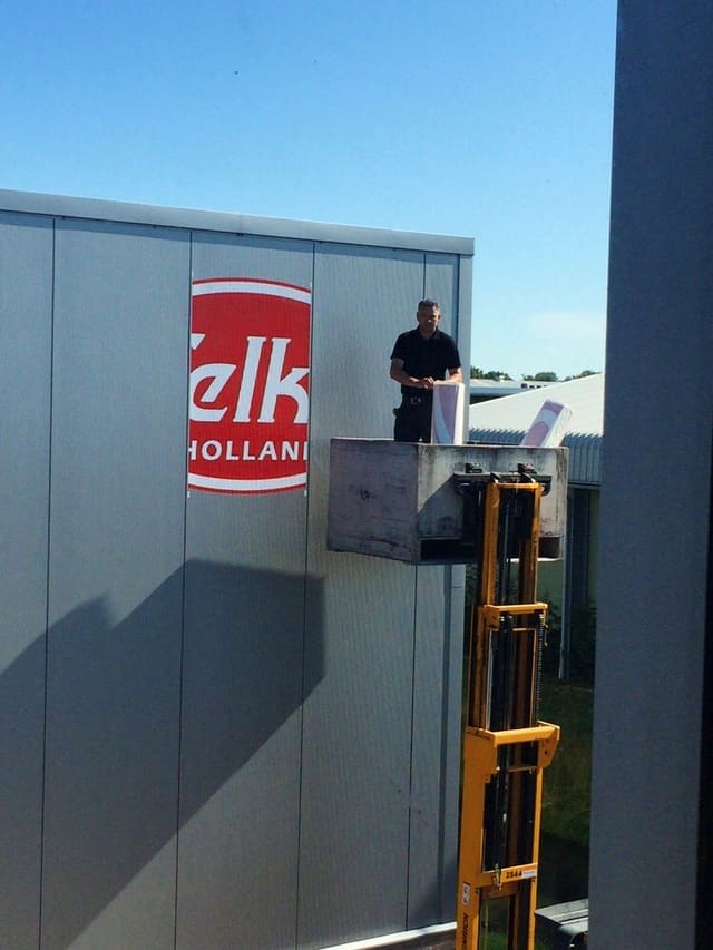 Logobord wordt op een bedrijfshal gemonteerd vanaf een werkplatform