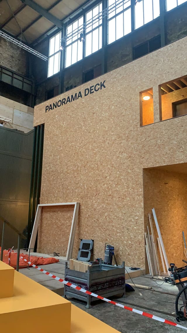 Donkere letters ‘Panorama Deck’ op een wand van OSB-platen in een industriële hal, tijdens de opbouw