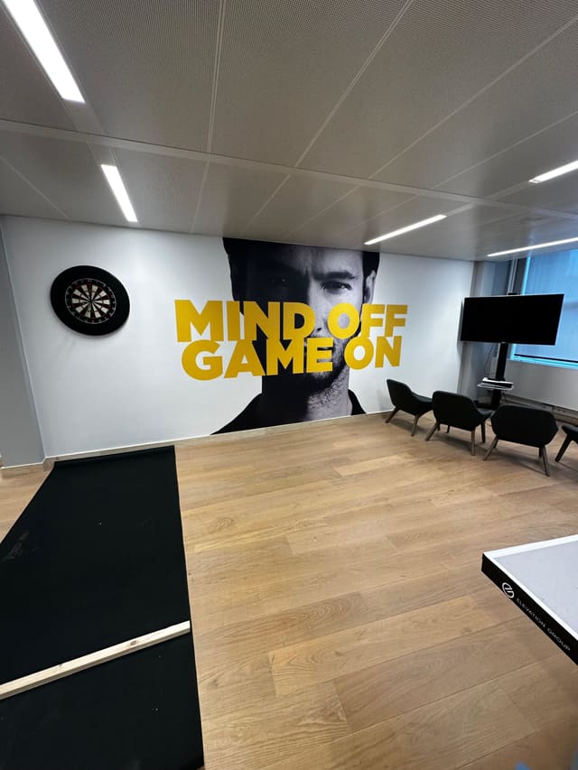 Wandvullende zwart-witprint van een man met de gele tekst ‘Mind off, game on’ in een ontspanningsruimte