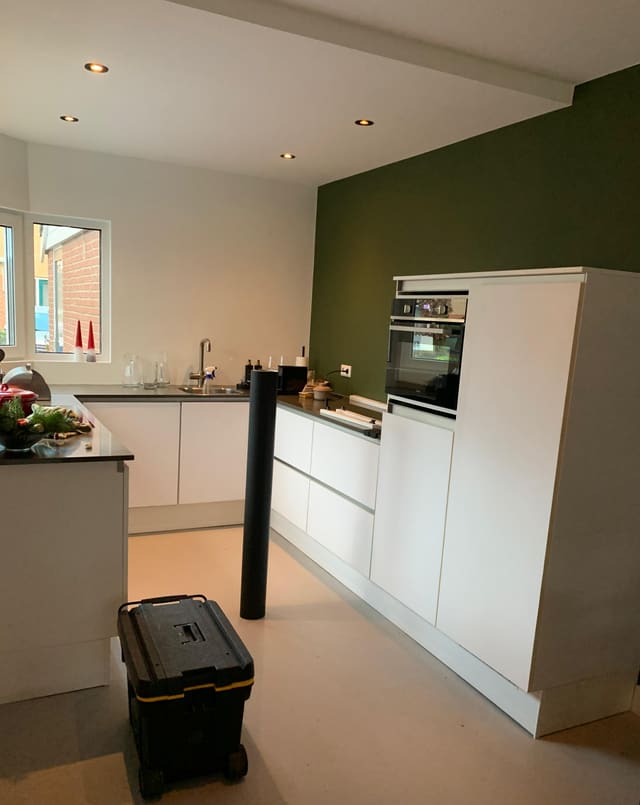 Witte keuken met een groene wand vóór het wrappen; een gereedschapskist staat klaar