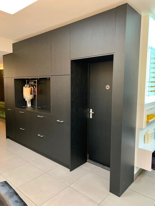 Kastenwand met nis en wc-deur in zwarte houtlook, in een kapsalon