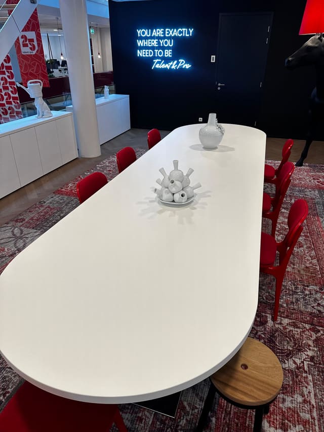 Lange witte tafel met ronde uiteinden en rode stoelen in een kantoor