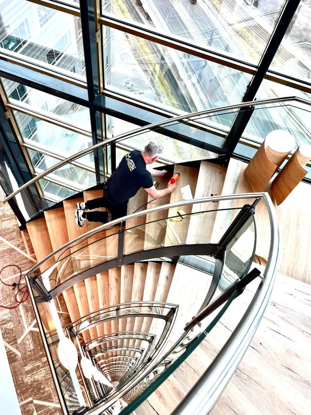 Folie wordt op de treden van een wenteltrap met een glazen balustrade aangebracht
