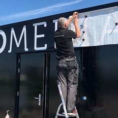Marco Elfrink op een trapje terwijl hij witte letters op een zwarte gevel plakt