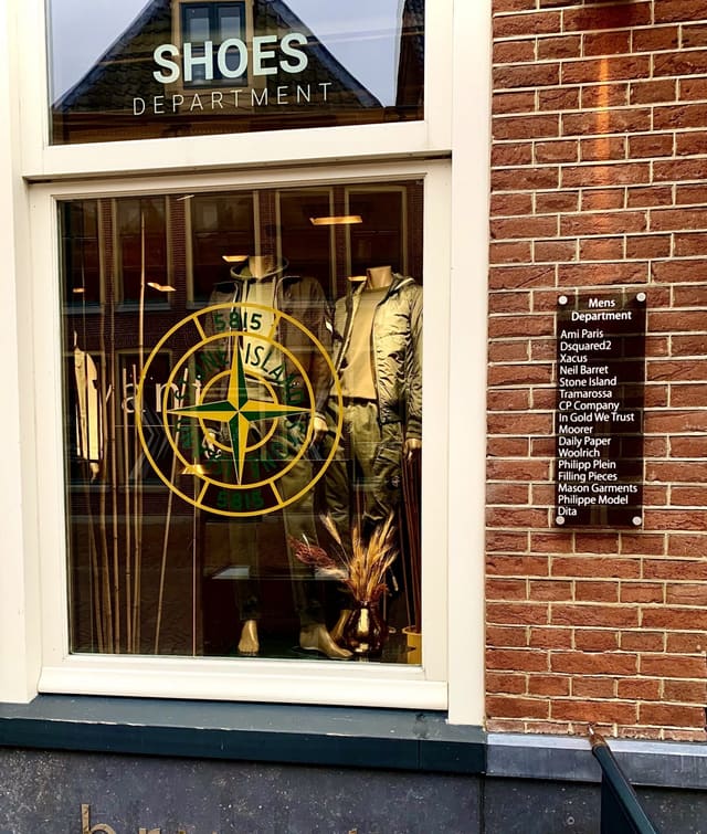 Etalage van een kledingzaak met goudkleurig logo op het glas