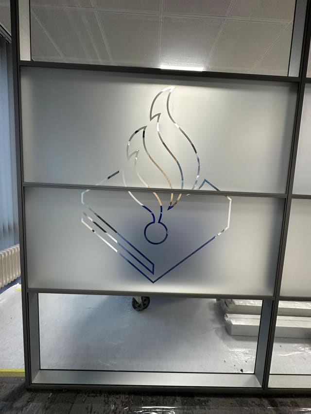 Een groot logo met een vlam, uitgespaard in matglasfolie op een glazen wand