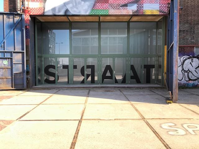 Grote zwarte letters over de hele glazen entreepui van een museum, gezien vanaf het plein