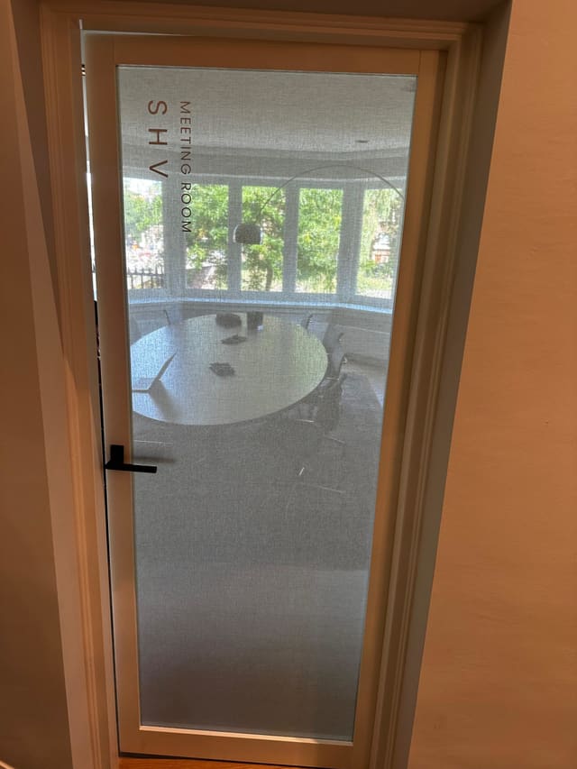 Deur van een vergaderruimte met matglasfolie en de naam verticaal op het glas