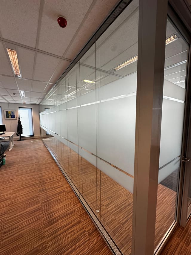 Glazen kantoorwanden met een band matglasfolie op ooghoogte, langs een kantoortuin