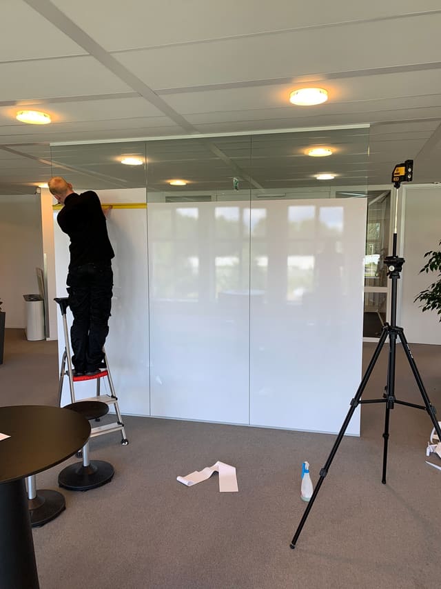Matte folie wordt vanaf een trapje op een glazen wand aangebracht