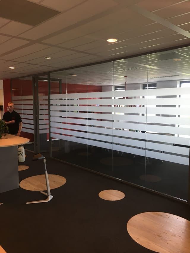 Glazen wand van een vergaderruimte met brede horizontale stroken matte privacyfolie