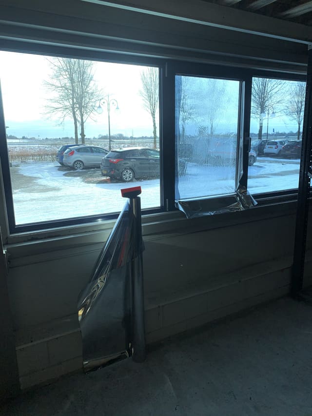 Zonwerende spiegelfolie wordt op een raam aangebracht, met de rol folie en een rakel ervoor
