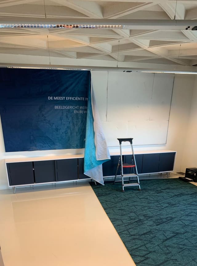 Blauw doek wordt in een smartframe boven een rij lage kasten gespannen