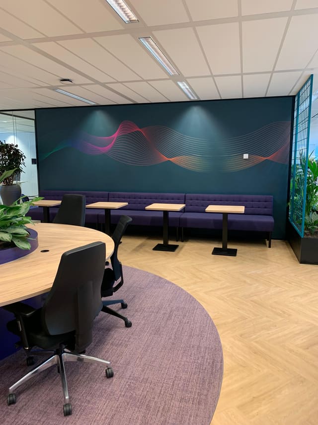 Kantoorruimte met een petrolblauwe wand vol gekleurde golflijnen achter een rij tafels