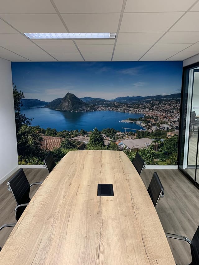 Vergaderkamer met een wandvullende foto van een meer tussen de bergen achter een lange tafel