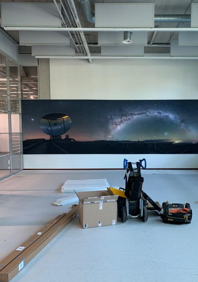 Breed smartframe met een foto van de Melkweg en een radiotelescoop in een kantoorruimte