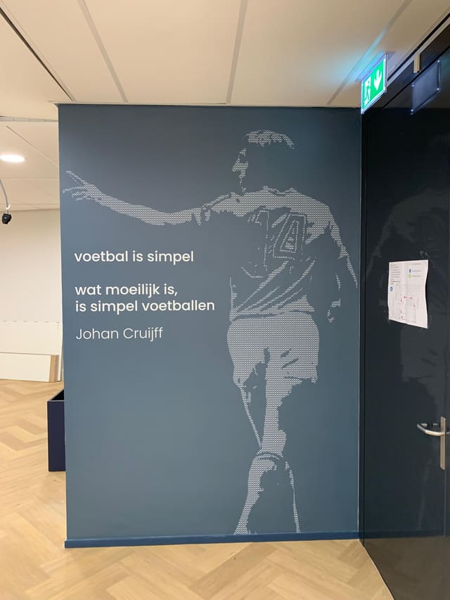 Blauwgrijze wand met een voetballer in lijnwerk en het citaat ‘Voetbal is simpel’ van Johan Cruijff