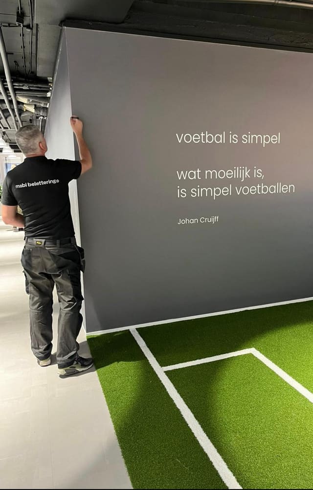 Marco plaatst een grijze wand met een voetbalcitaat boven kunstgras