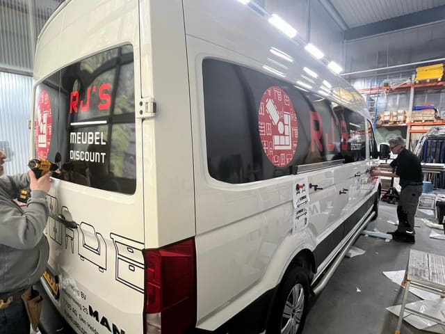 Belettering wordt op de zijkant van een witte bedrijfsbus aangebracht