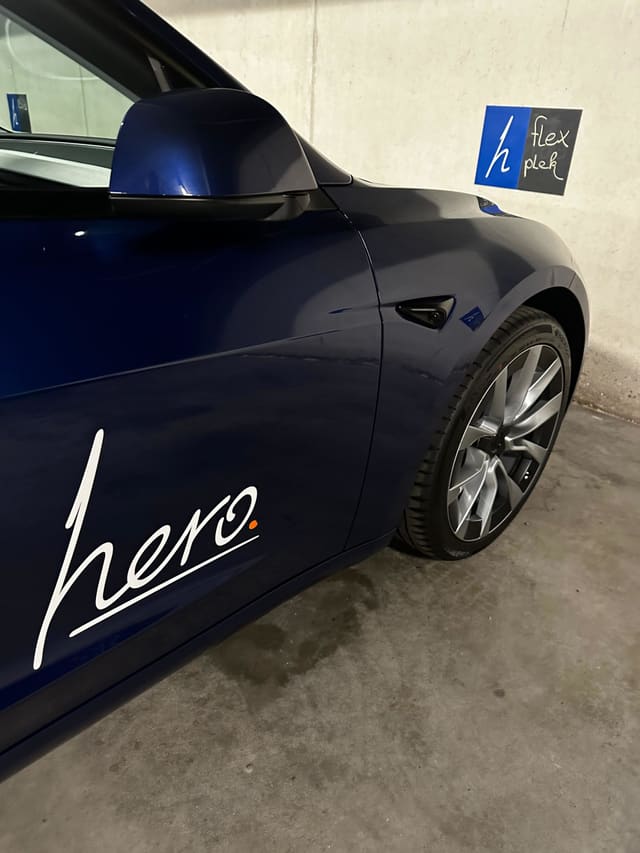 Donkerblauwe auto met een wit handgeschreven logo op het portier