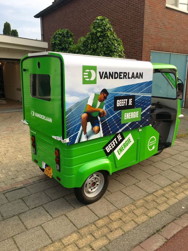 Groene elektrische tuktuk met op de laadbak een fotoprint van zonnepanelen en het logo